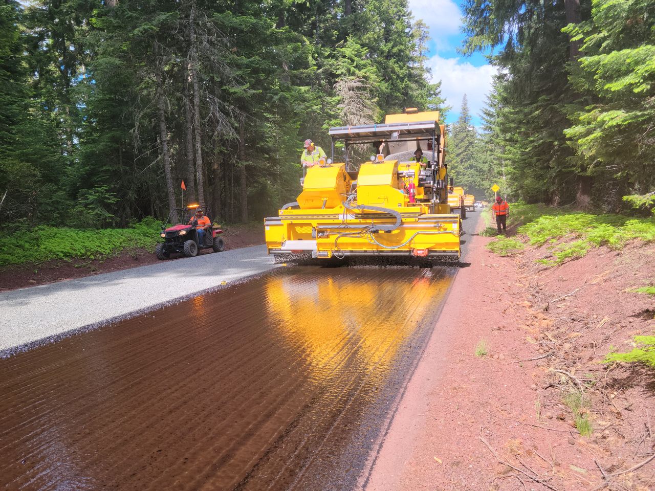 Paving machine working on a road through Mount Hood forested area.