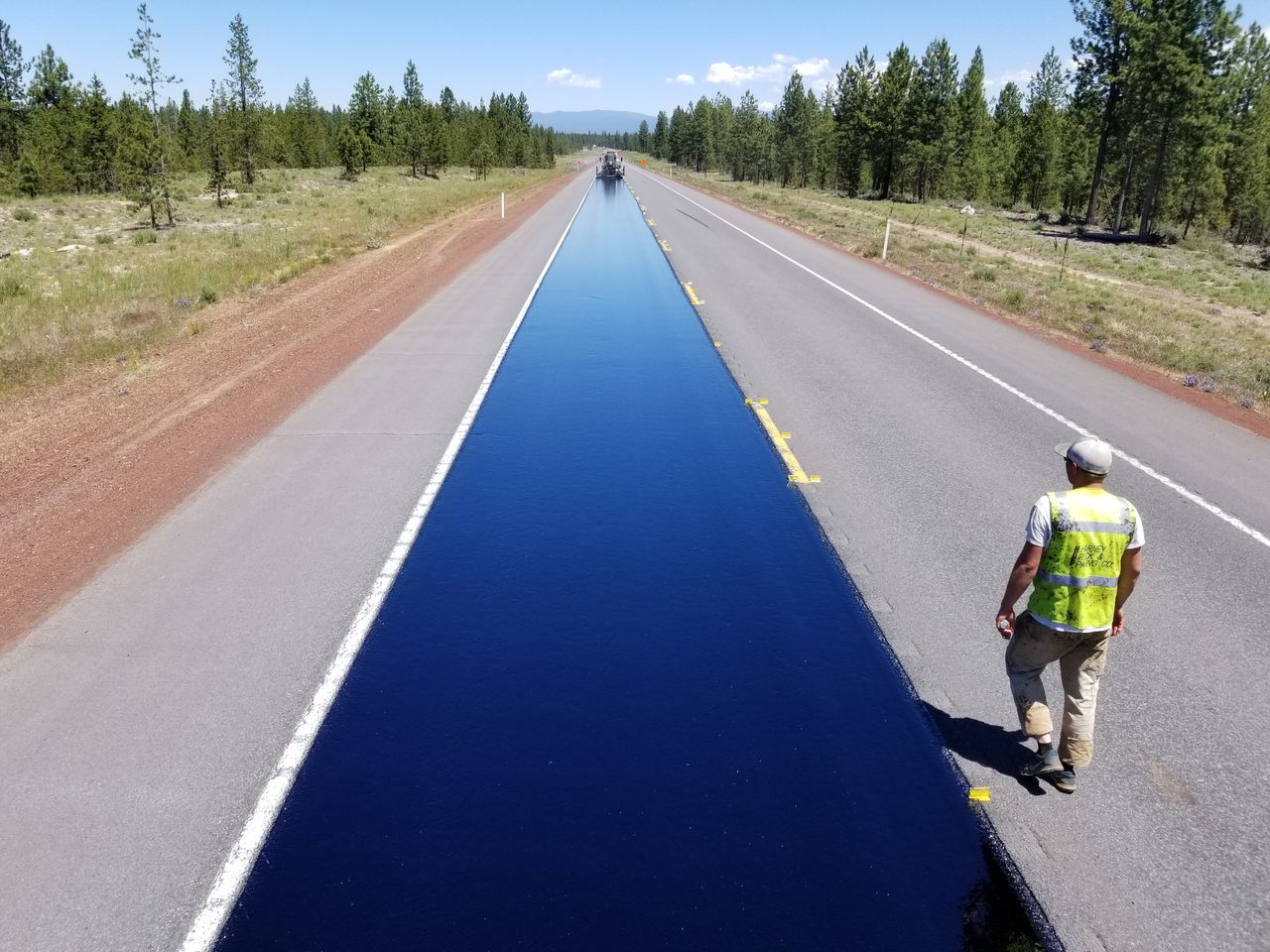 Drone shot of a highway under construction near La Pine, Oregon, featuring a worker and fresh asphalt.