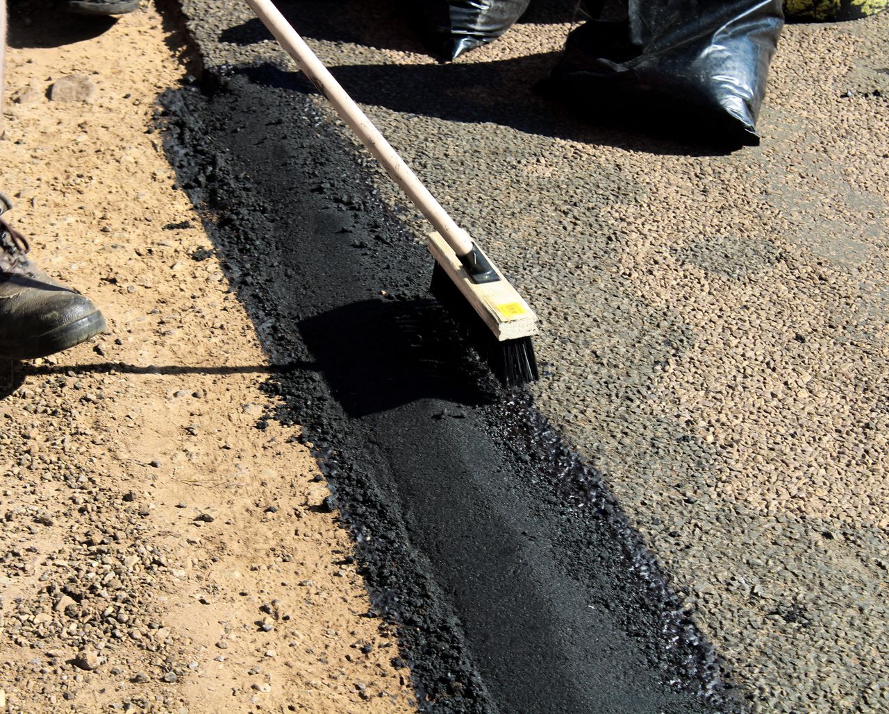 Detailed view of road maintenance with asphalt and worker tools in daytime.