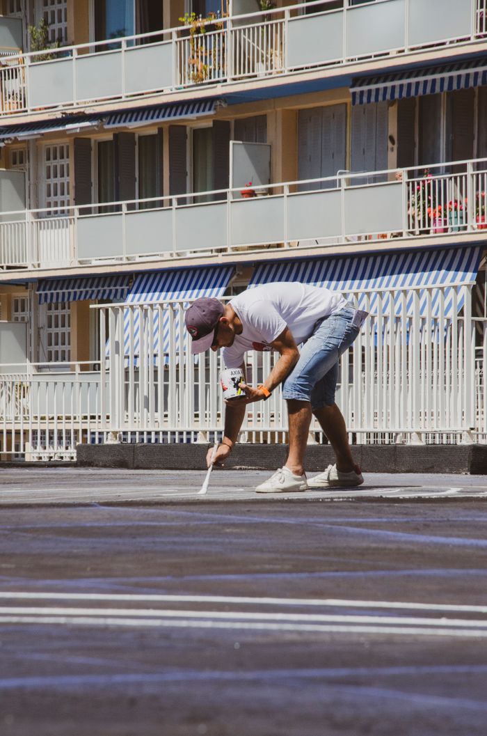 Man painting lines in a sunny Marseille parking lot as part of urban maintenance work.
